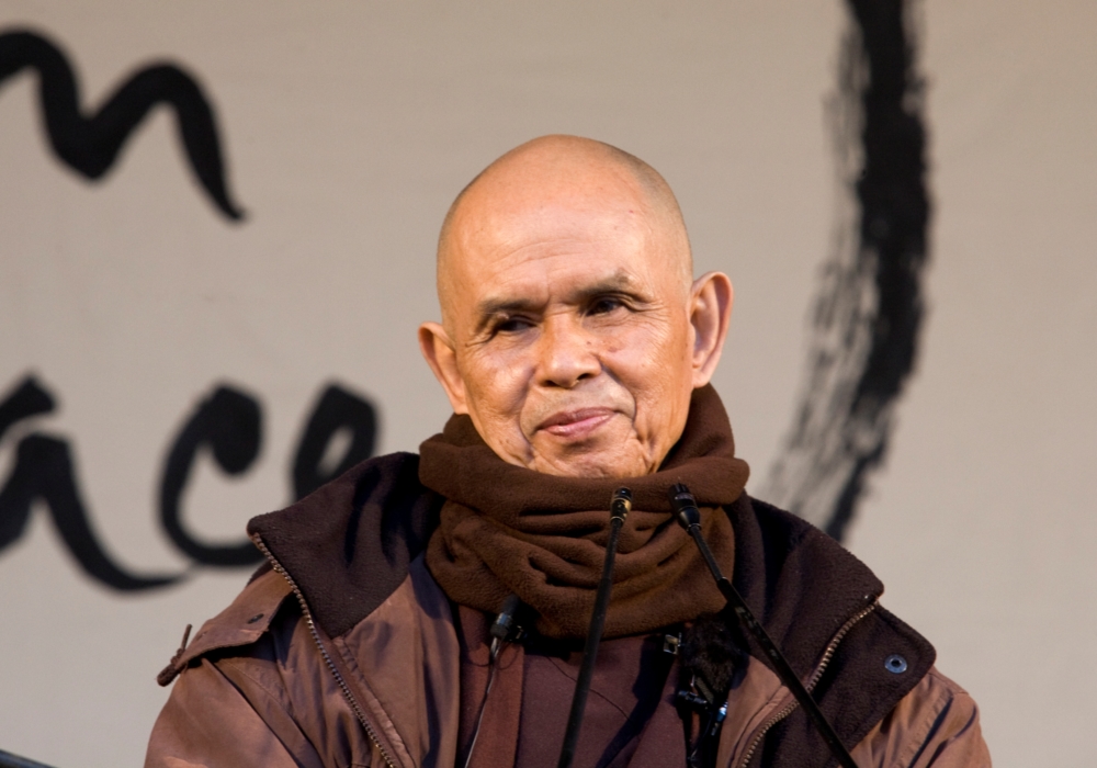 Thich Nhat Hanh warm ingepakt op een podium voor een enorme kalligrafie.