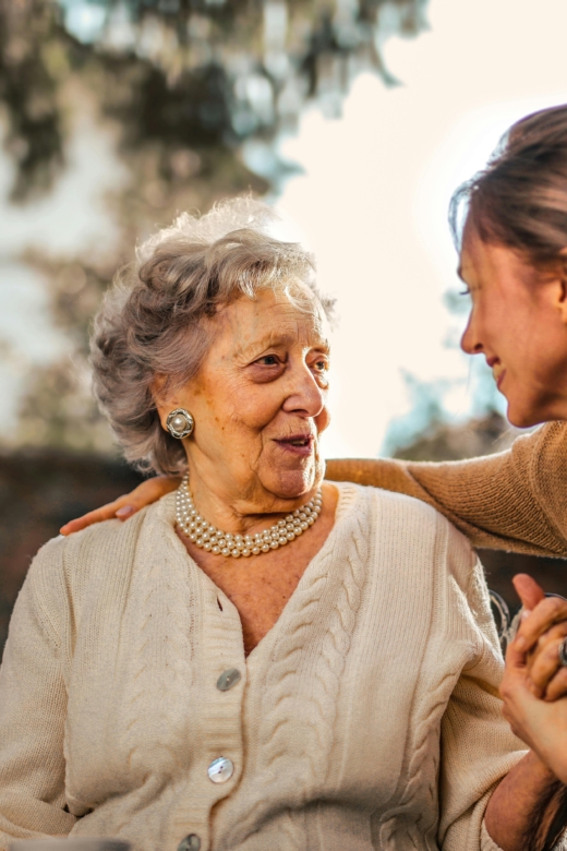 Elderly woman and adult daughter share a joyful, affectionate moment in a sunny garden.