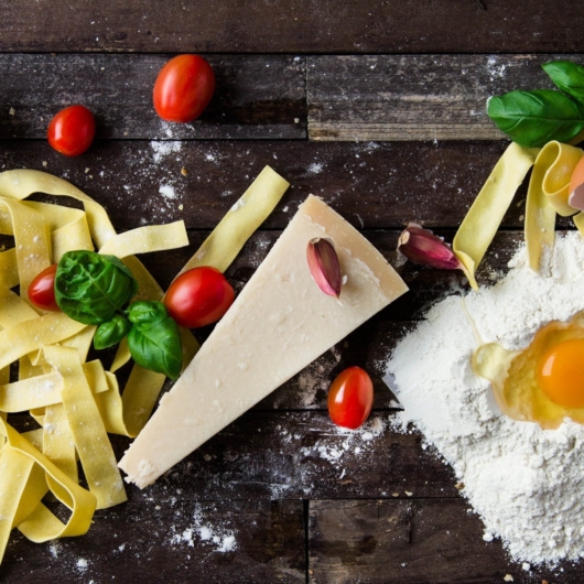 Werkblad met verse pasta, ei, meel, roma kerstomaat en basilicum